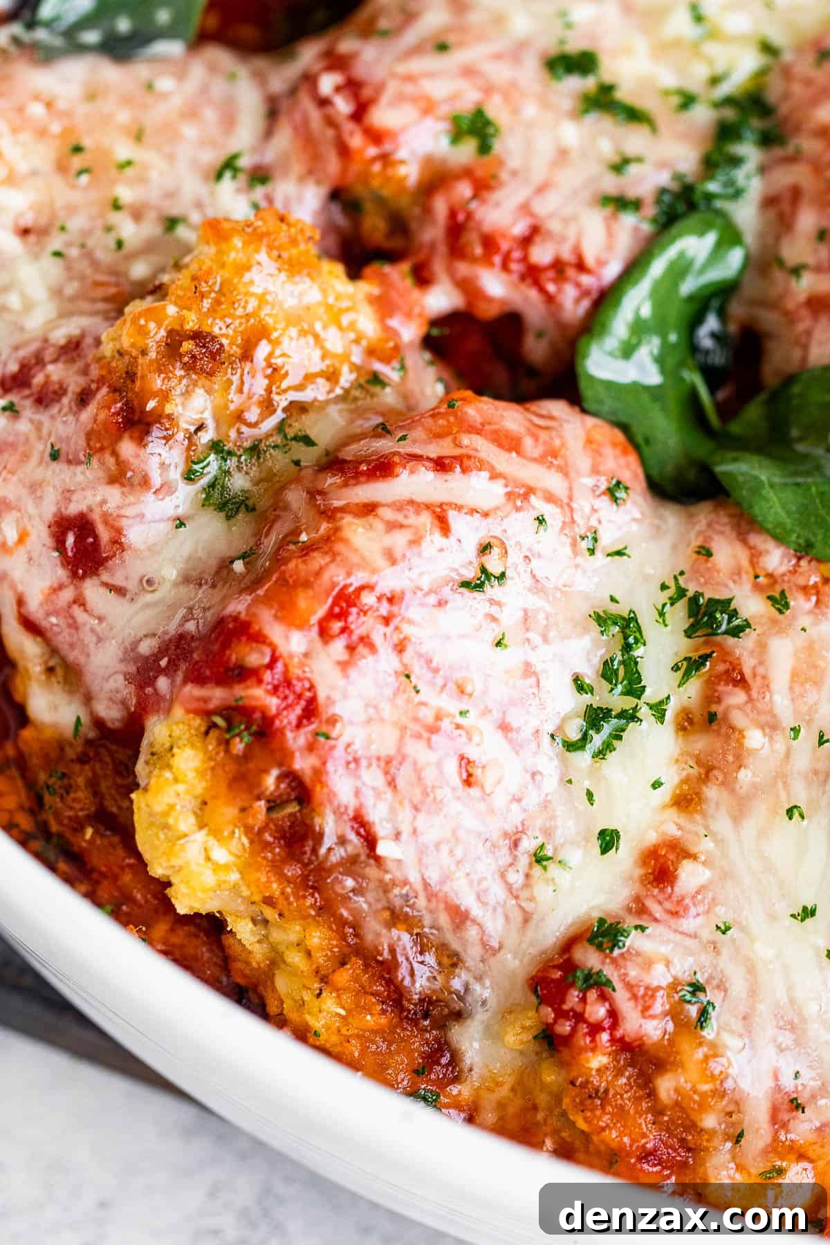 Close-up shot of a single serving of baked pork parmigiana, showcasing the golden-brown crust, rich sauce, and melted cheese, garnished with fresh basil.