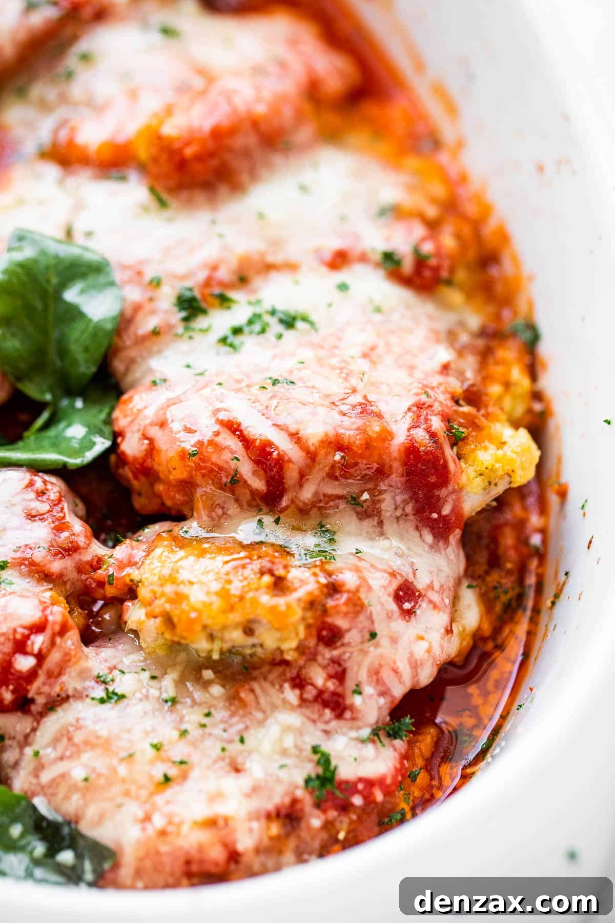 Close-up side shot of a serving of baked pork parmigiana, highlighting the layers of breaded pork, sauce, and melted cheese, garnished with basil.
