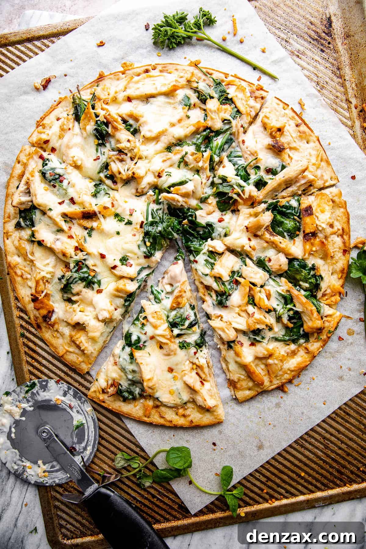 overhead shot of homemade chicken alfredo pizza with pizza cutter placed next to the pizza