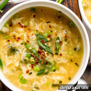 An inviting overhead shot of a bowl of Egg Drop Soup, garnished with vibrant green onions and a sprinkle of red pepper flakes, highlighting its comforting appeal.