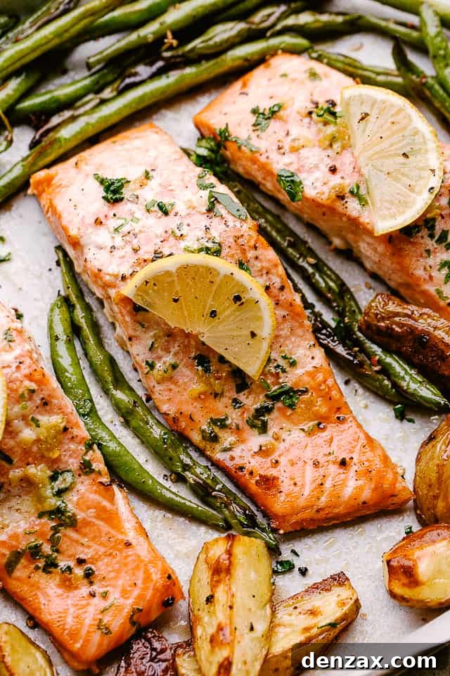 Close-up of baked salmon fillets glistening with lemon-garlic butter, alongside tender roasted green beans and golden potatoes.