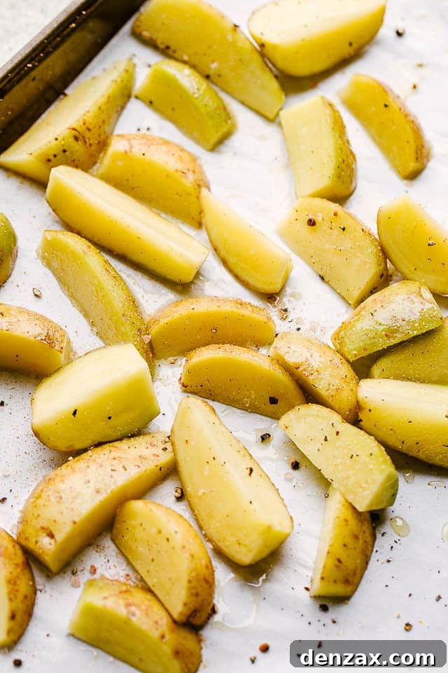 Close-up of quartered Yukon gold potatoes being seasoned with olive oil, salt, and pepper on a baking sheet before roasting.