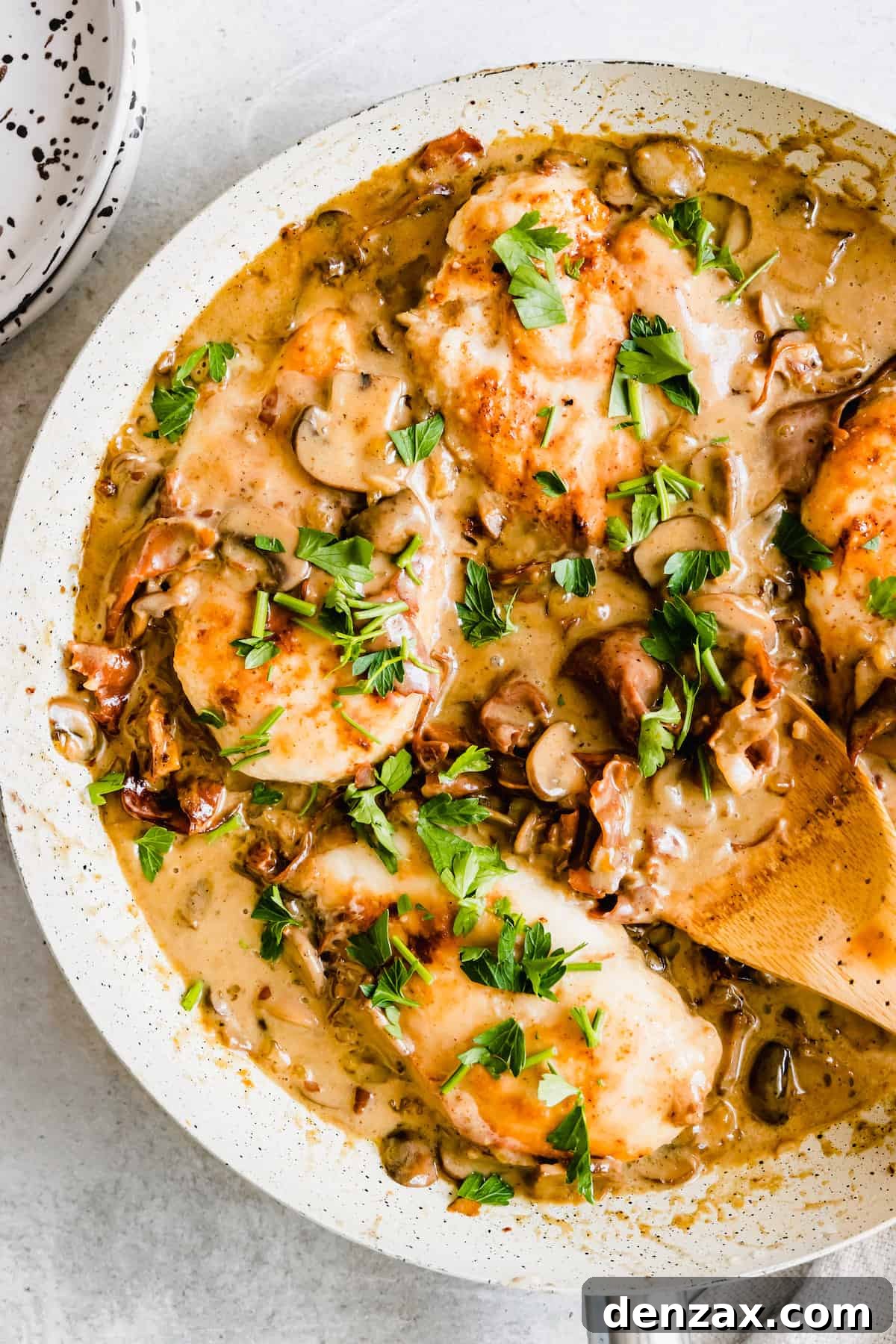Chicken marsala in a white pan with a wooden spoon