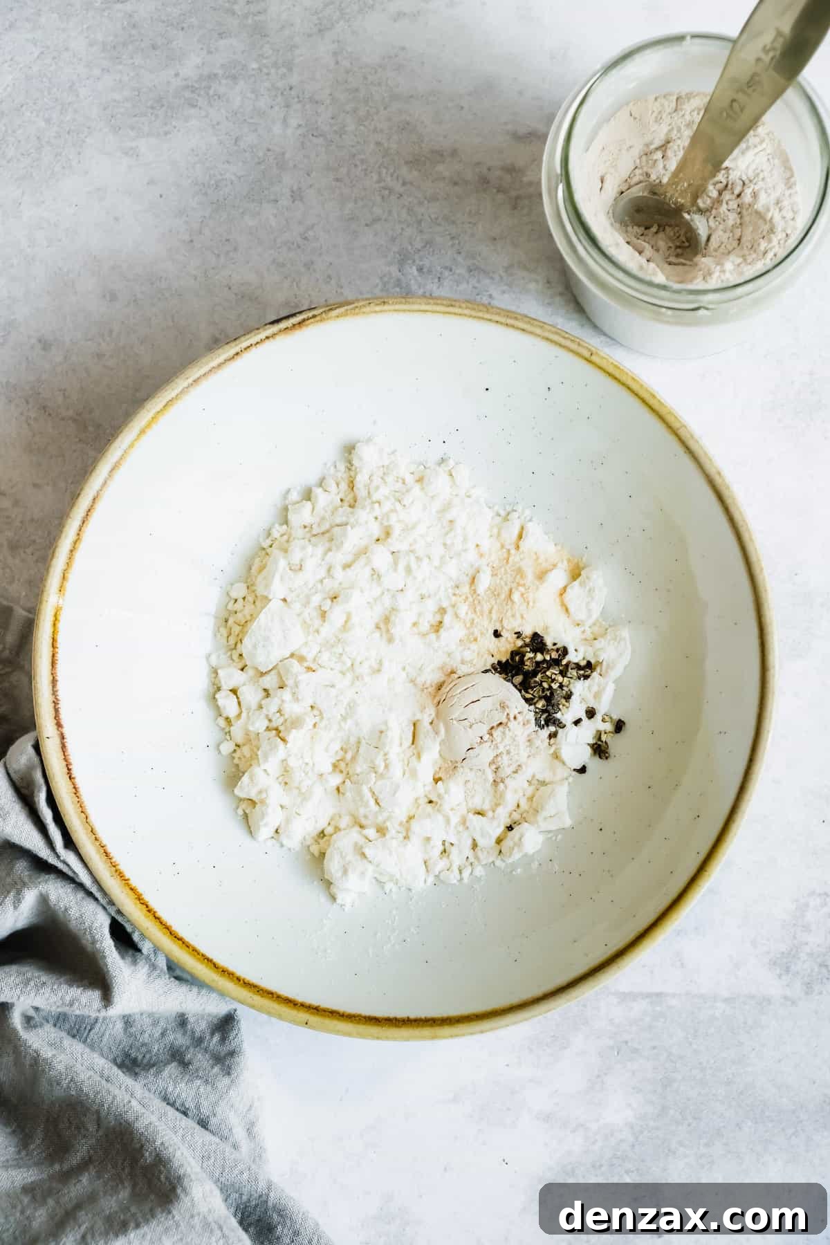 A small white bowl filled with all-purpose flour, garnished with freshly crushed black pepper, ready for thickening the stew.