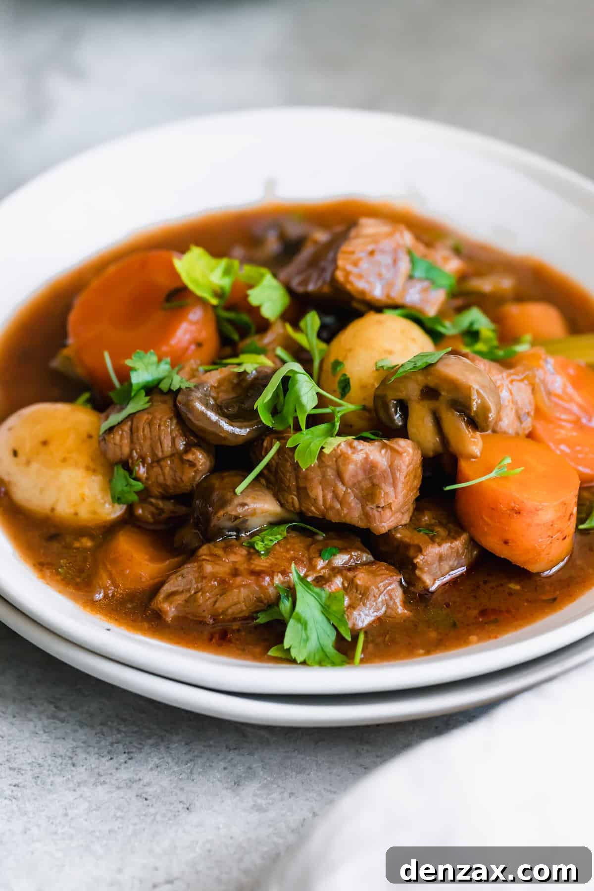 A white bowl brimming with Hearty Guinness Beef Stew, garnished with fresh herbs and featuring visible carrots and potatoes.