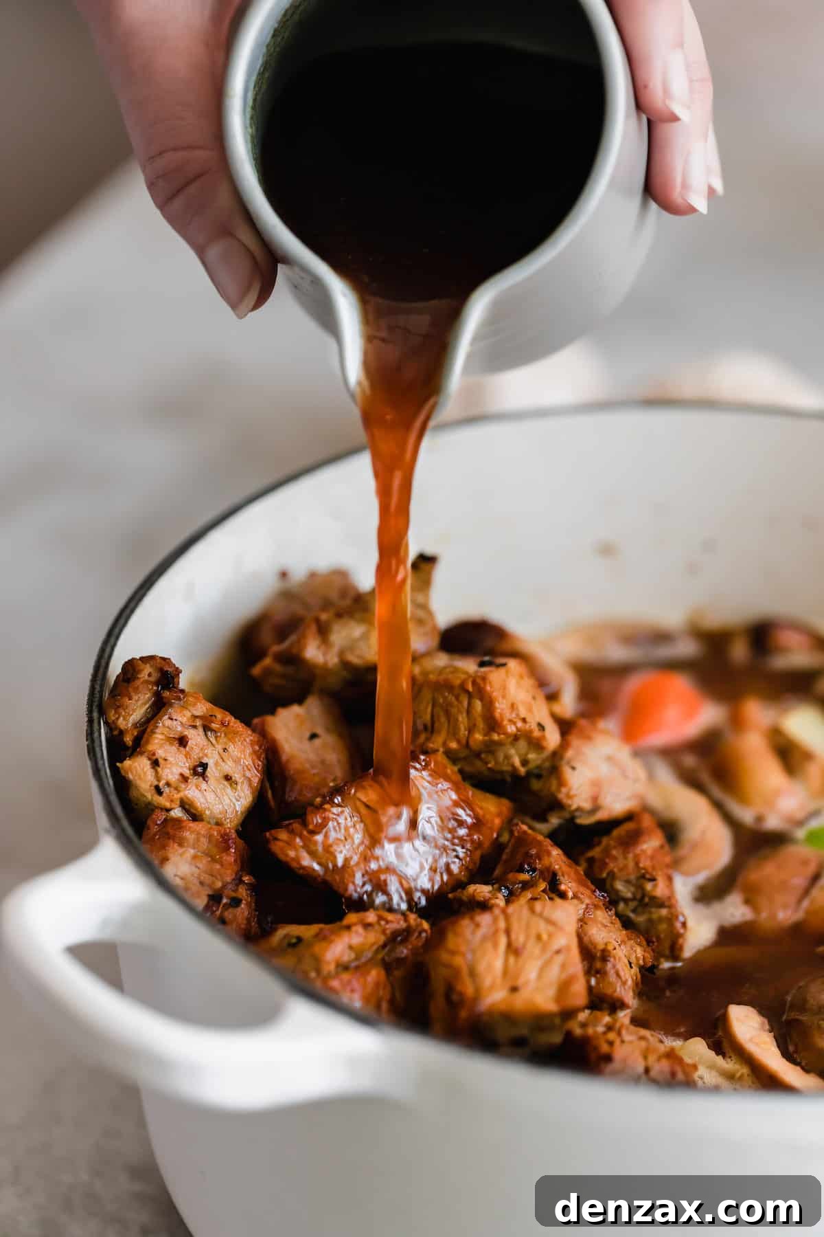 A bottle of Guinness beer being poured into a large pot of beef stew, infusing it with rich, dark stout flavor.