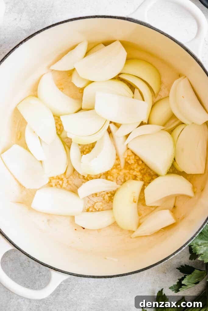 Finely chopped onions and minced garlic gently sautéing in a pan, forming the aromatic foundation for the stew.