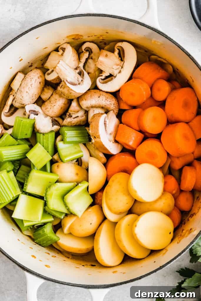 A colorful medley of chopped raw celery, carrots, onions, potatoes, and mushrooms patiently awaiting their turn in the soup pot, illustrating the vibrant vegetable component of the stew.