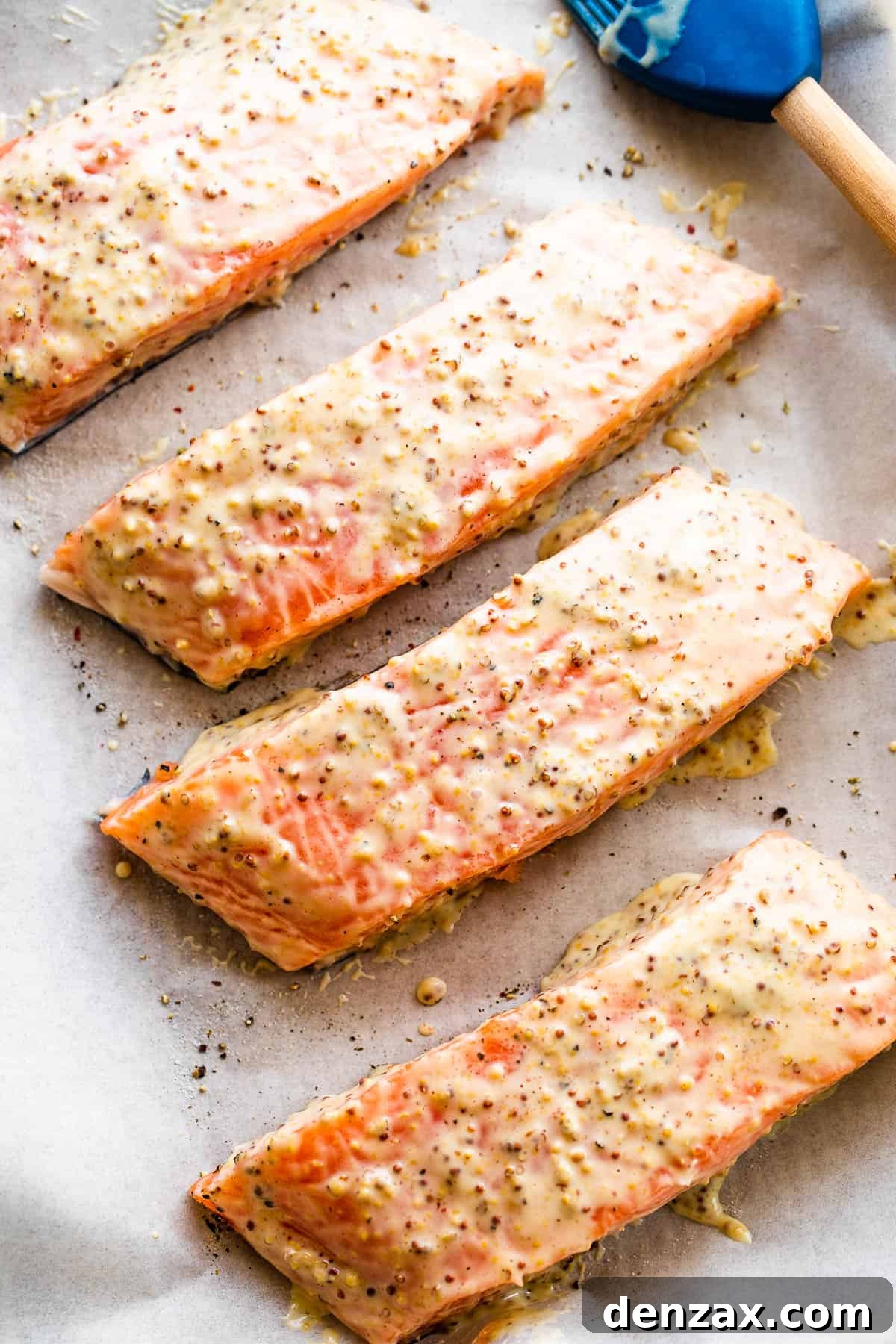This baked Maple Mustard Salmon recipe is lightly seasoned, then brushed with a sweet and tangy sauce made from maple syrup and Dijon mustard! four raw salmon fillets arranged on a baking sheet