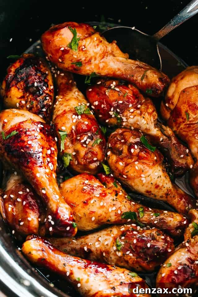 Close up of perfectly glazed chicken drumsticks with a glistening honey sriracha sauce, garnished with sesame seeds and fresh cilantro.