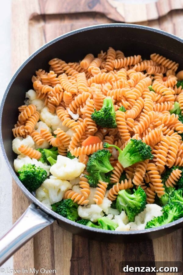 Fresh broccoli florets and chopped carrots and cauliflower cooking in a saucepan, beginning to soften.