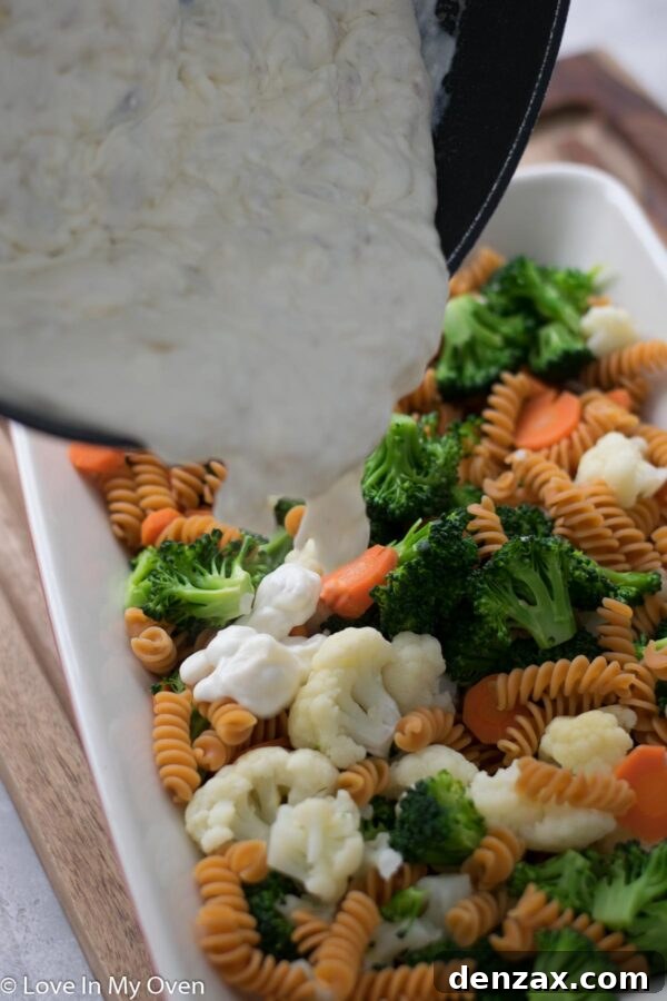 Cream cheese cubes melting into a rich white sauce in a saucepan, creating a smooth, thick consistency.