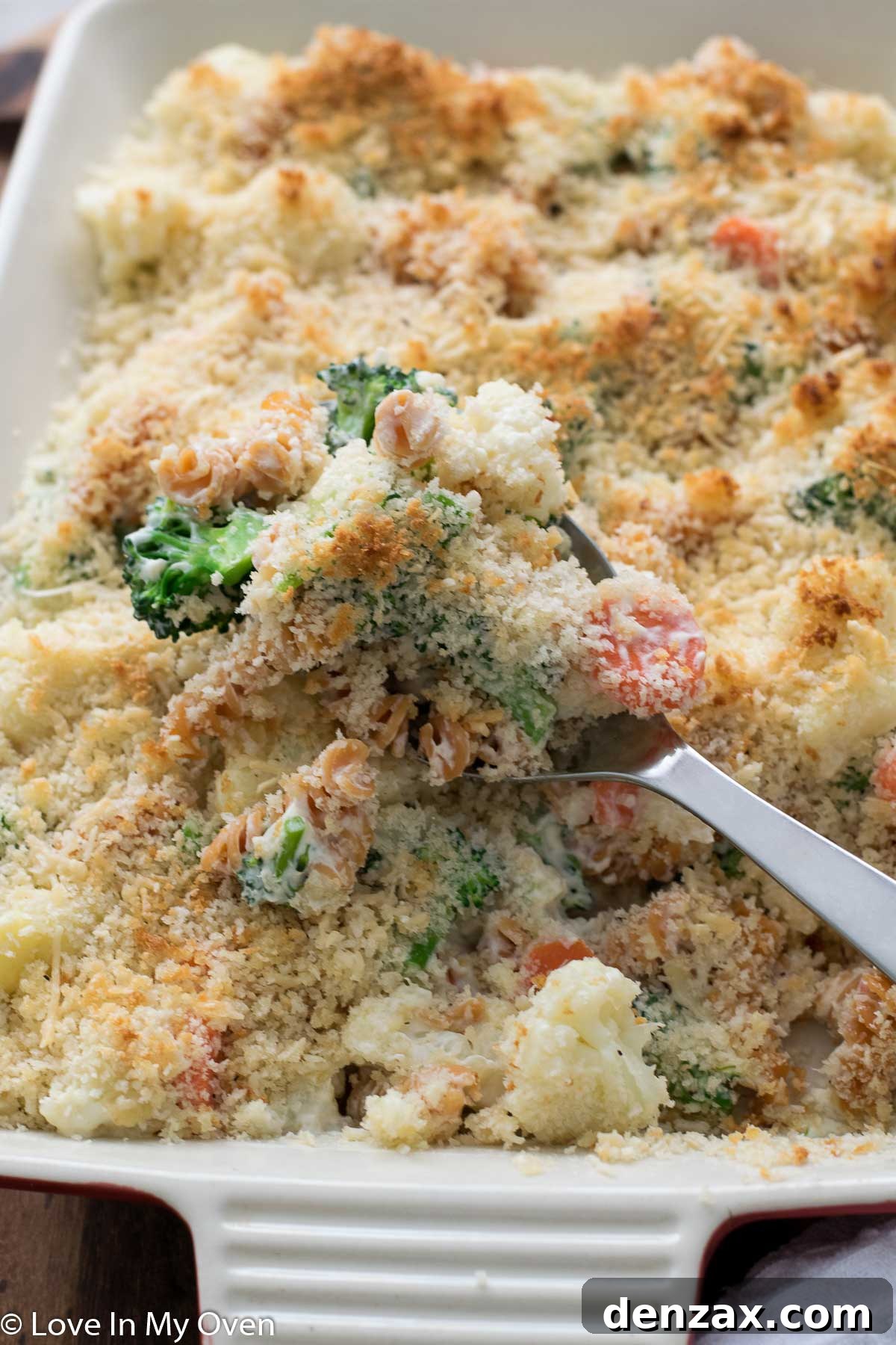 Serving spoon scooping a portion of the baked creamy vegetable casserole from the dish, showing the rich sauce and tender vegetables.