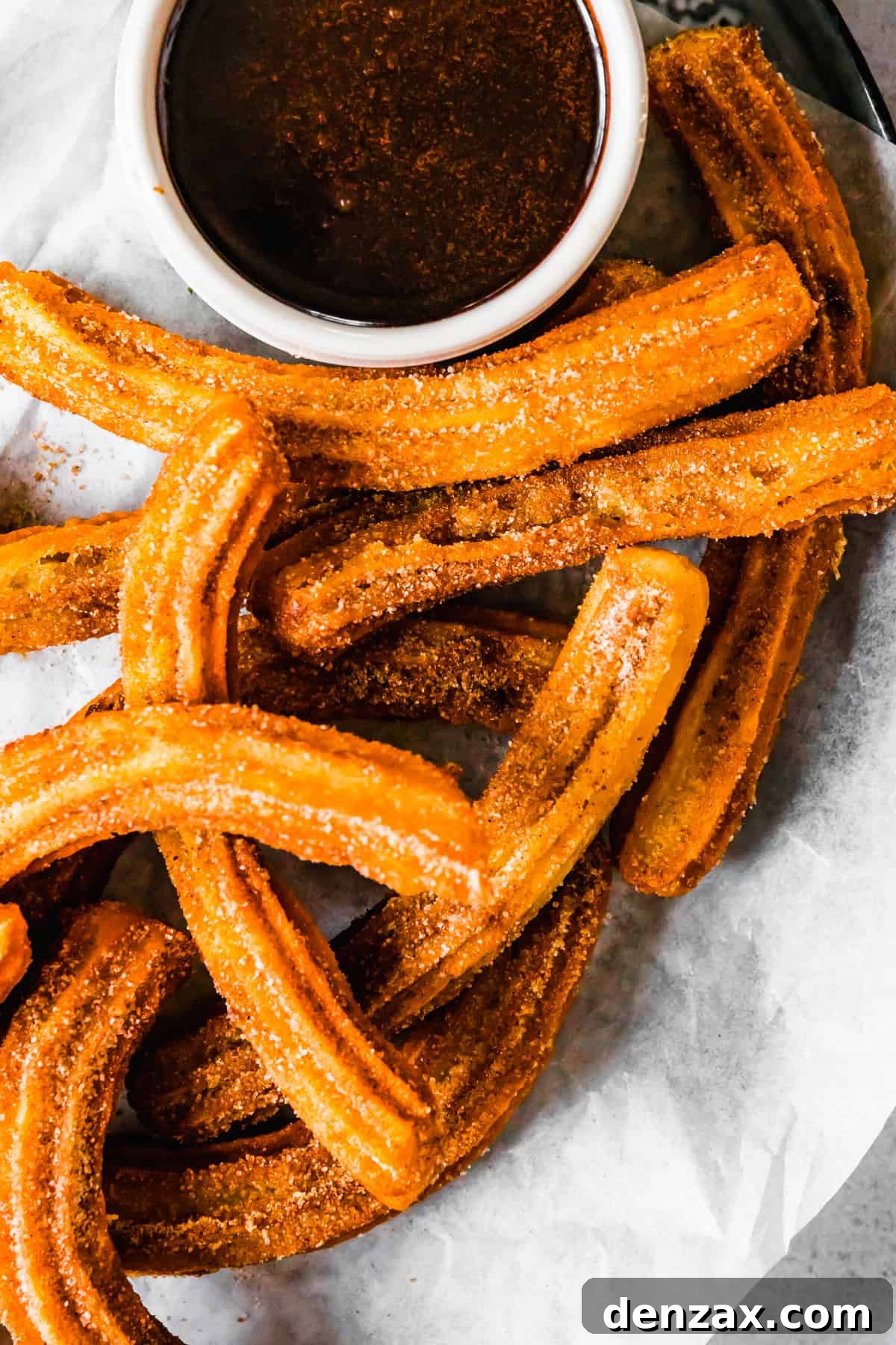A bountiful plate of homemade churros, coated in cinnamon sugar, alongside a bowl of rich chocolate dipping sauce. Recipe by Easy Weeknight Recipes.