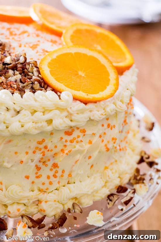 Tall three-layer Orange Carrot Cake with thick cream cheese frosting, garnished with pecans.