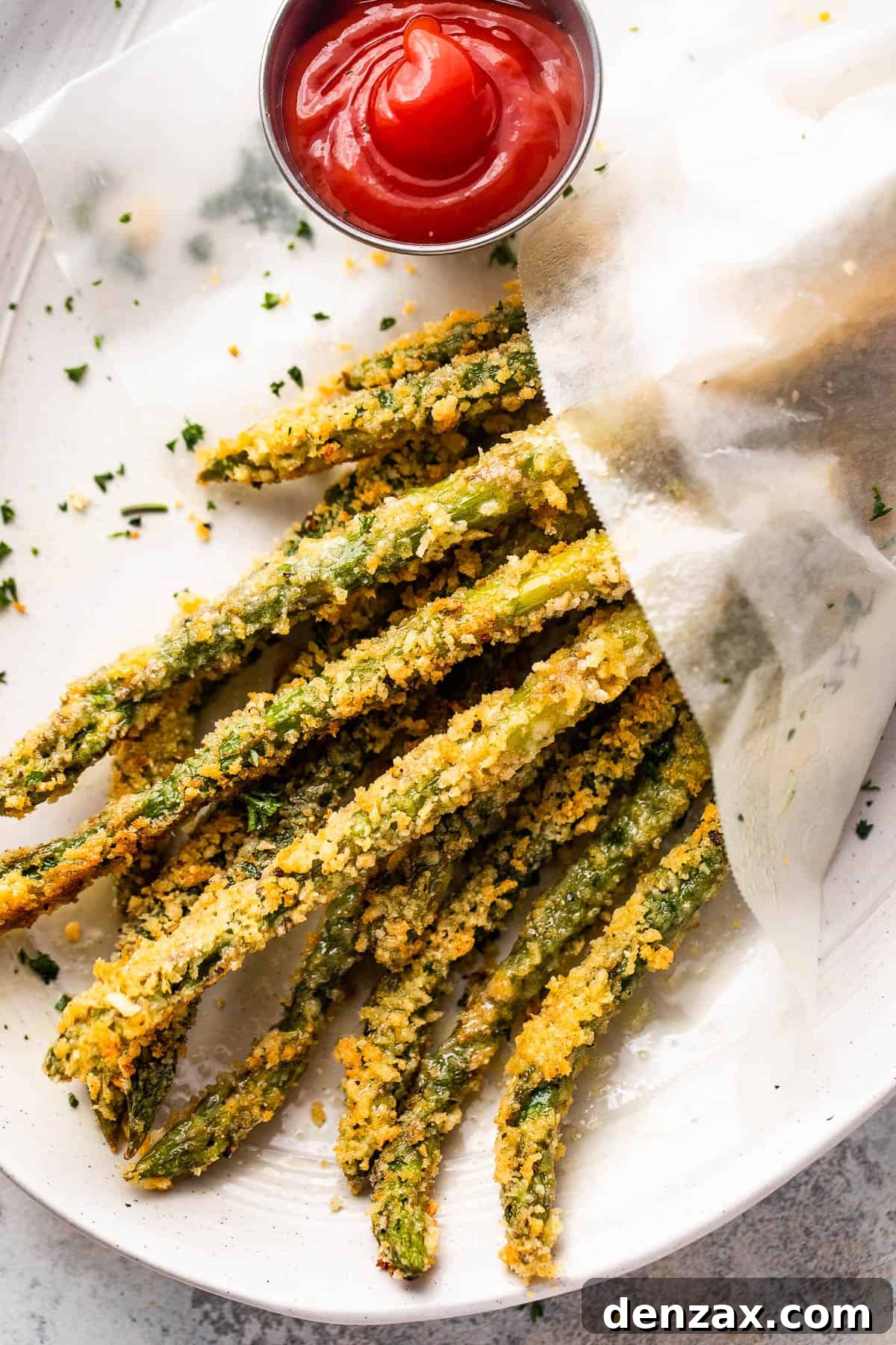 Overhead shot of golden-brown baked parmesan panko asparagus fries served with a ramekin of ketchup on the side, ready for dipping.