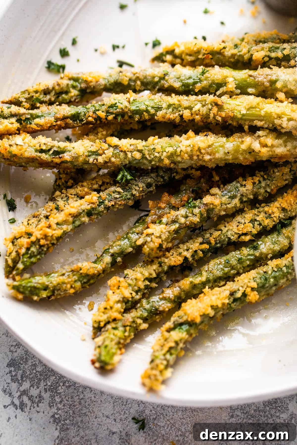 Close-up of several perfectly baked parmesan panko asparagus spears, golden brown and crisp, artfully arranged on a serving plate.