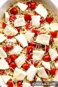 Chicken Caprese casserole in a white baking dish topped with fresh mozzarella chunks and cherry tomatoes before baking.