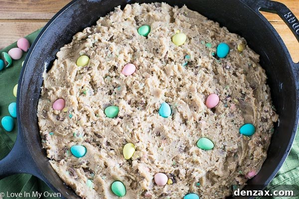 Adding crushed mini eggs to cookie dough in a bowl, preparing for baking in a skillet