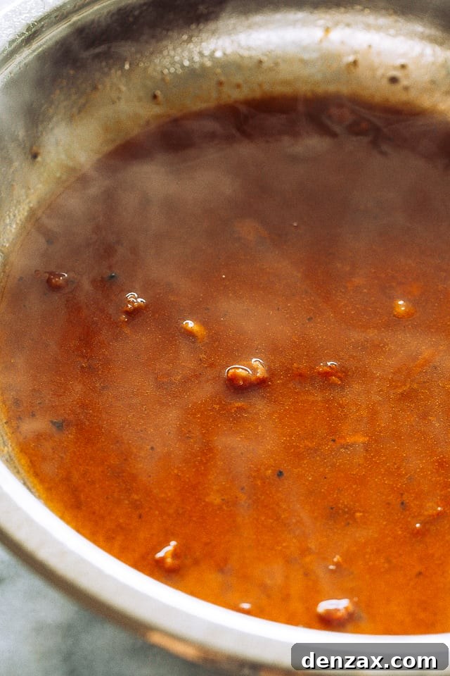 Pineapple barbecue sauce simmering in a skillet, thickening to a rich, glossy consistency.