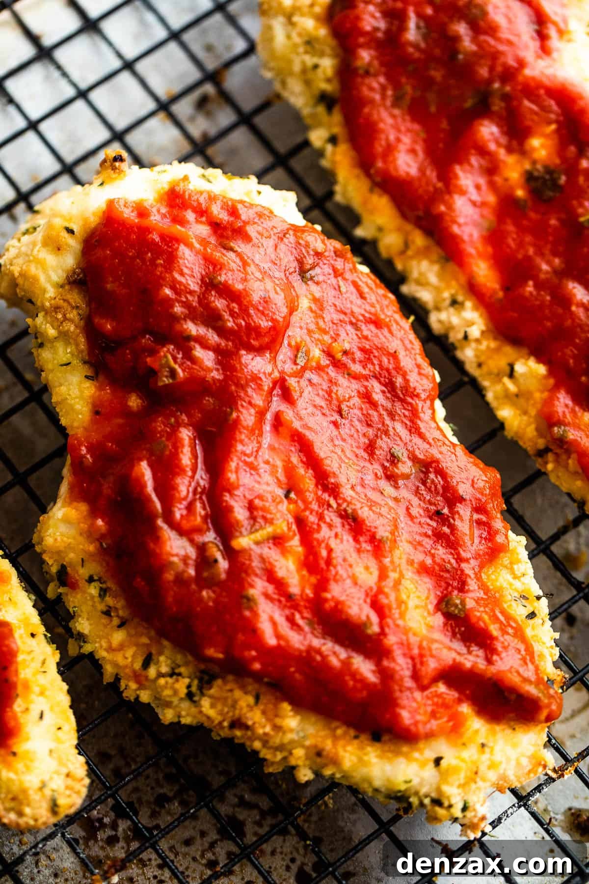 Two Pieces of Partially Cooked, Breaded Chicken with Marinara Sauce Spread on Top