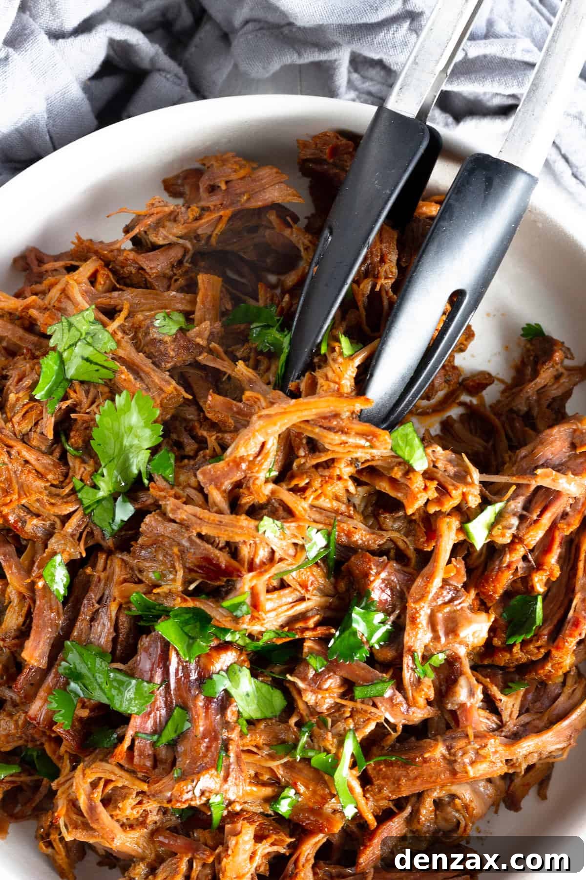 A white bowl brimming with succulent Instant Pot Beef Barbacoa, garnished with fresh parsley, ready to be enjoyed.