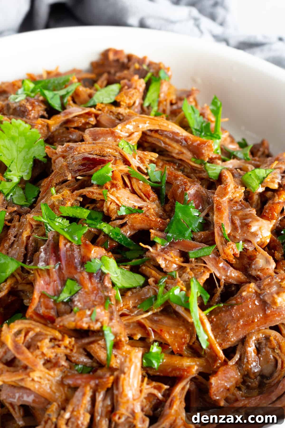 A close-up shot of perfectly tender Instant Pot Beef Barbacoa filling a white bowl, showcasing its rich texture and irresistible juices.