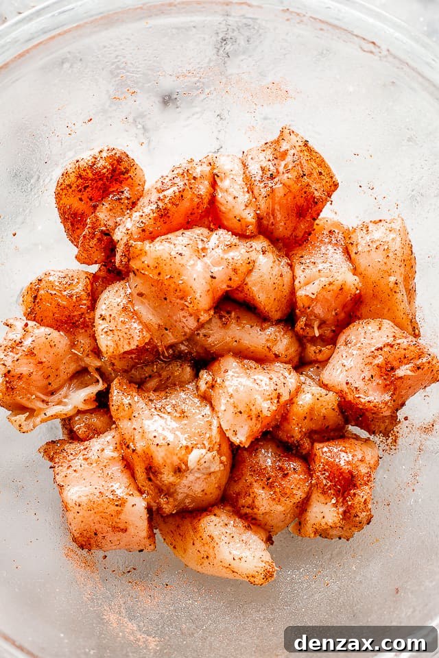 Raw cubes of chicken breast seasoned generously with taco seasoning in a bowl, ready for cooking.
