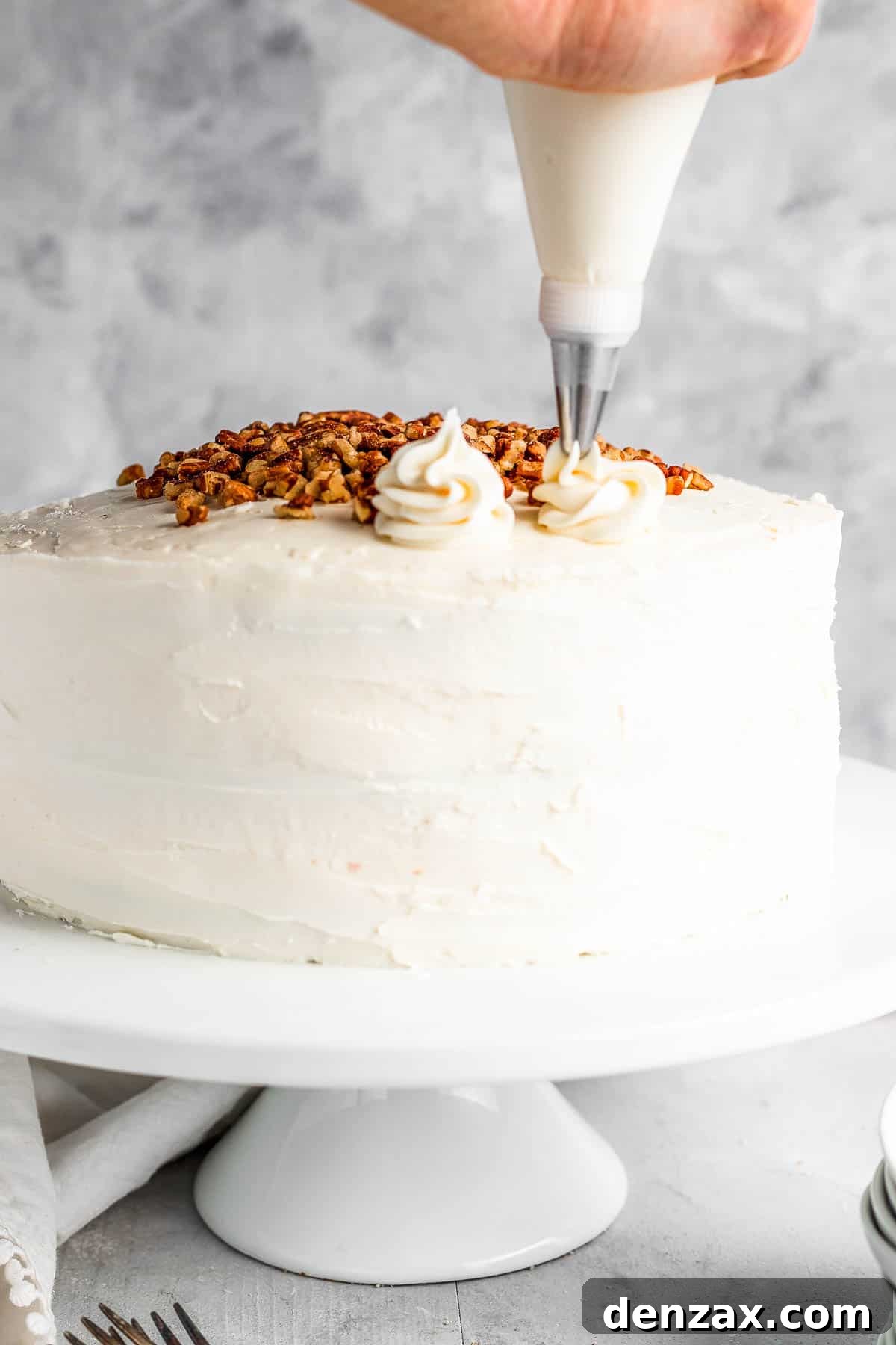 A Piping Tip Adding Swirls of Cream Cheese Icing Onto the Frosted Cake