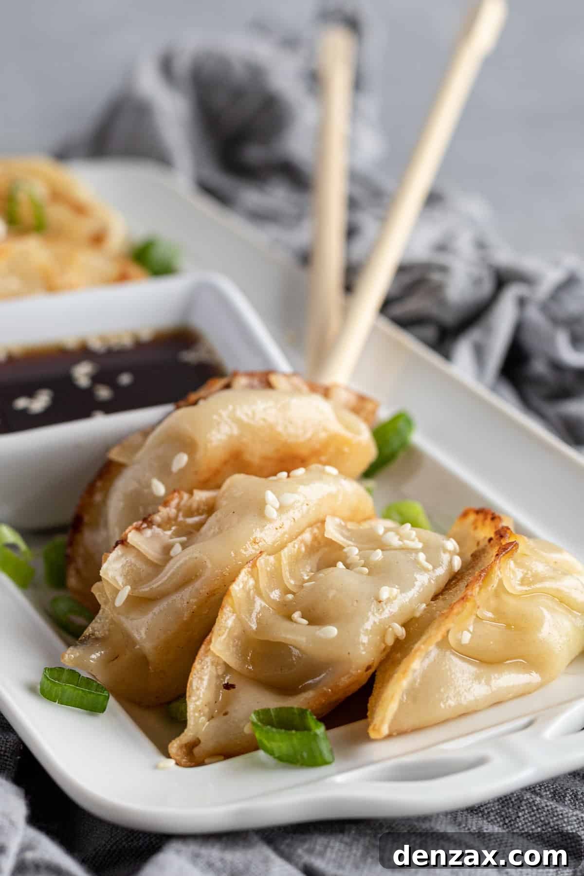 Four chicken potstickers on a serving platter with two chopsticks in the background