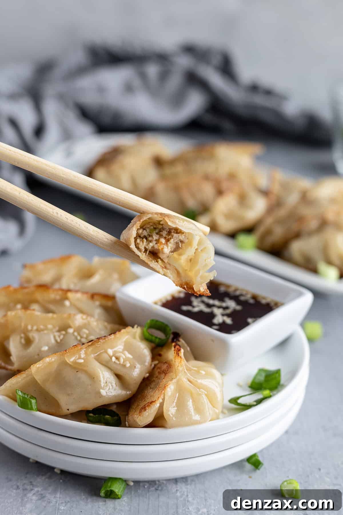 A Chicken Potsticker being held by a pair of wooden chopsticks