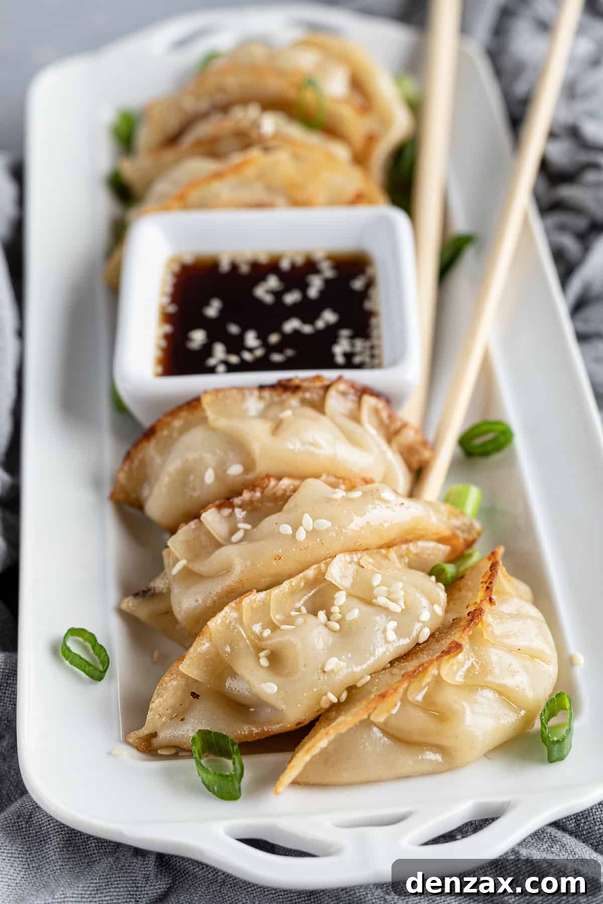 Seven chicken dumplings on a serving platter with dipping sauce and chopsticks
