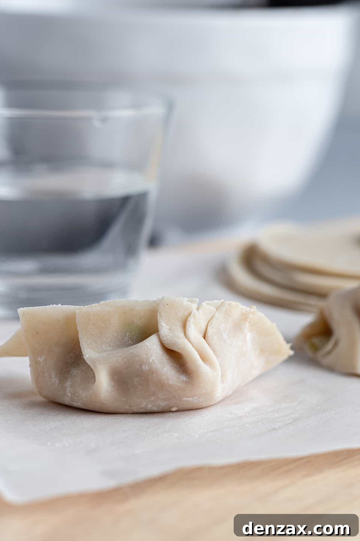 A filled and sealed dumpling beside a cup of water