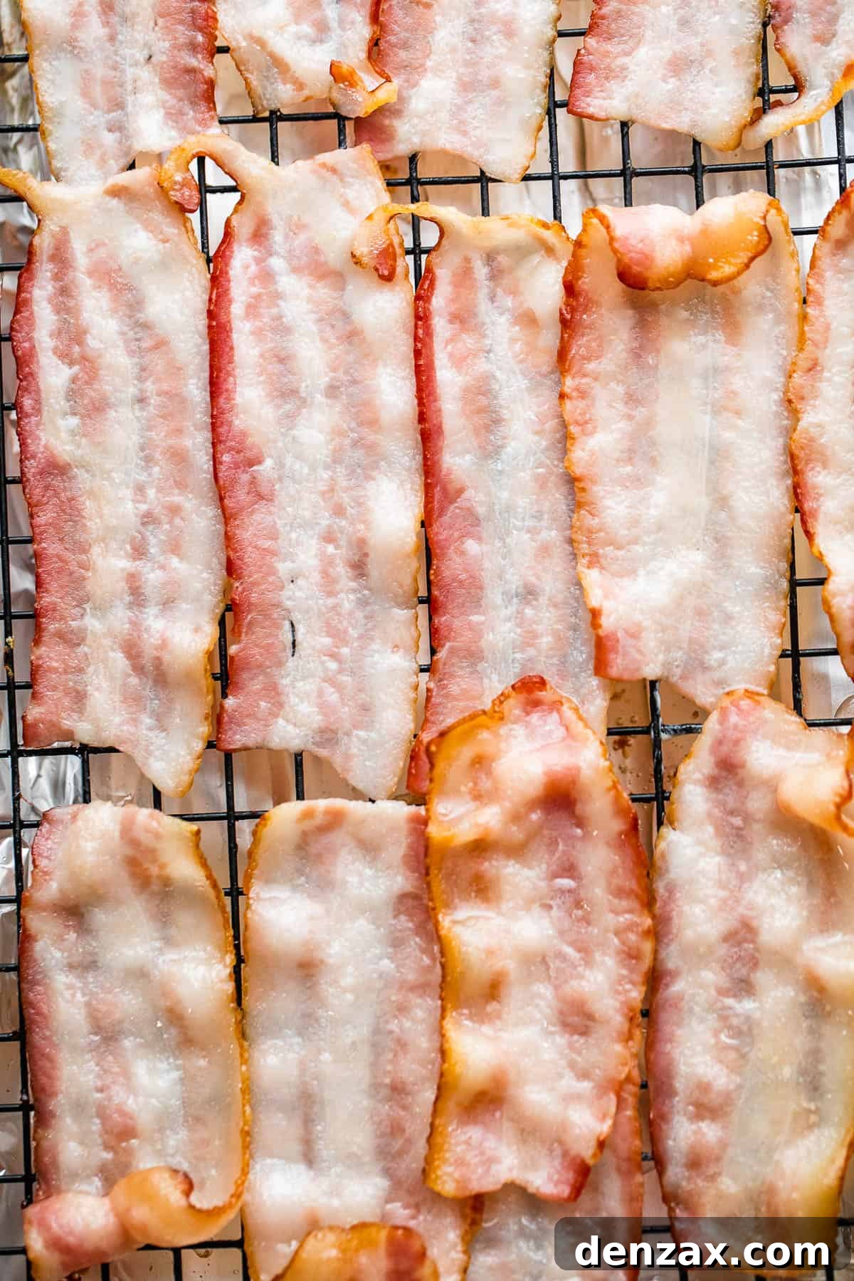 Halved strips of bacon neatly arranged on a wire rack over a foil-lined baking sheet, prepared for par-cooking before wrapping the shrimp.