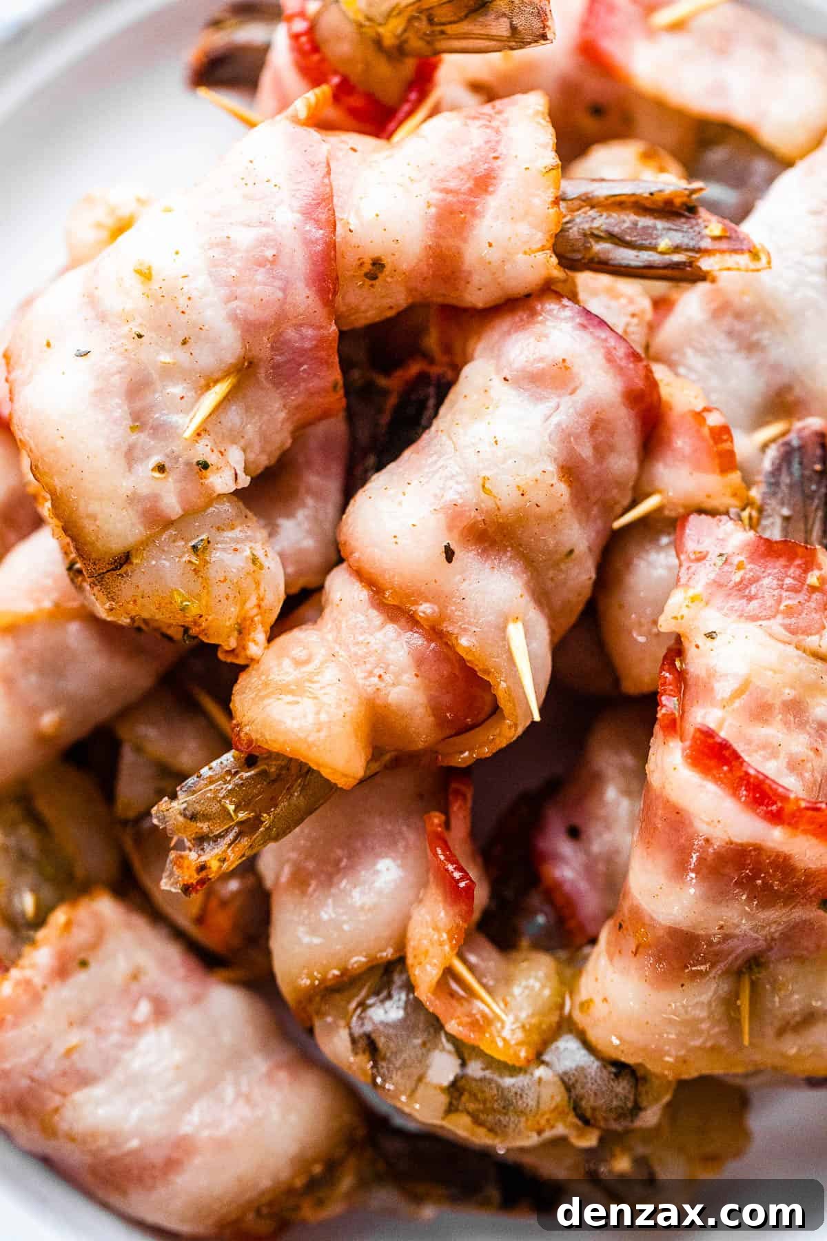 Raw jumbo shrimp individually wrapped in par-cooked bacon and secured with toothpicks, ready for grilling.
