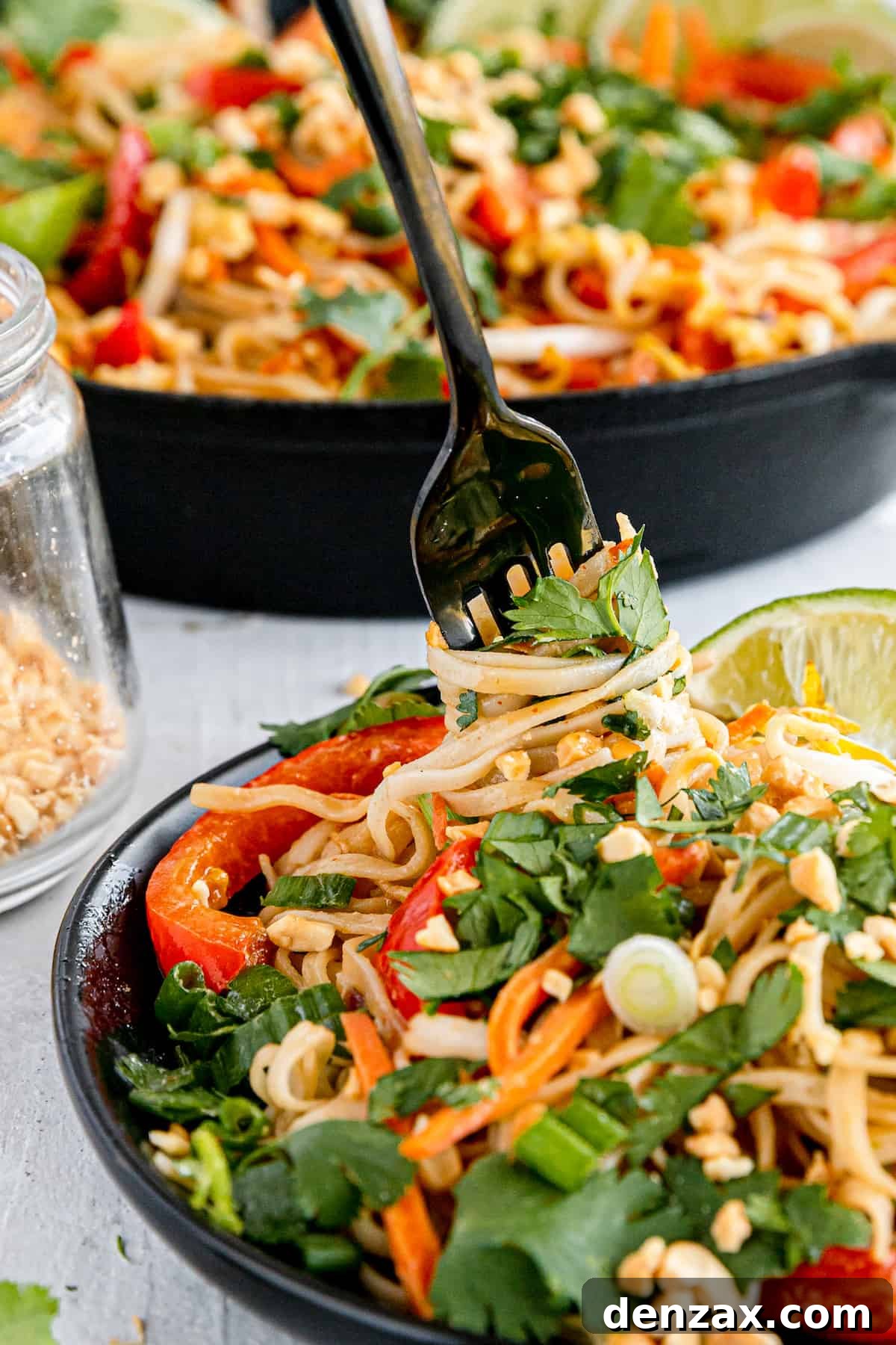 A Close-Up Shot of a Fork Digging Into a Plate of Pad Thai