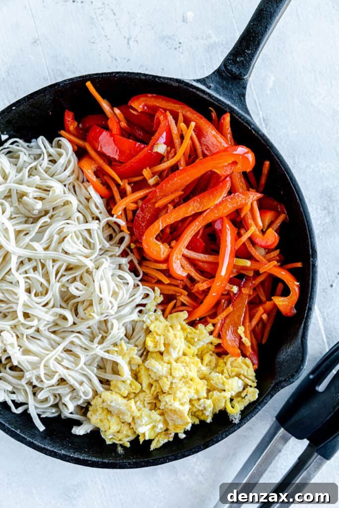 Scrambled Eggs, Brown Rice Noodles and Chopped Veggies Inside of a Black Skillet