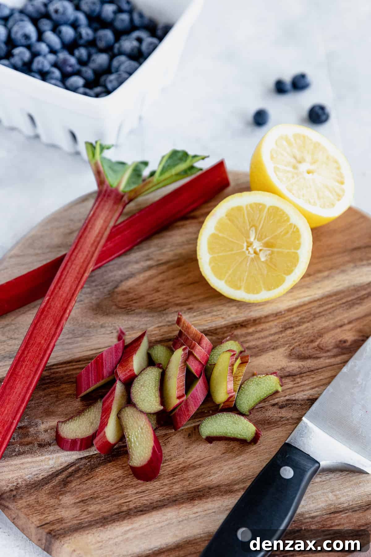 Chopped Rhubarb and a Halved Lemon on a Cutting Board with a Bowl of Blueberries in the Background, showcasing fresh ingredients