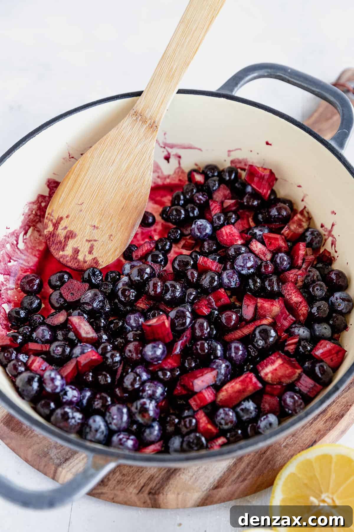 The vibrant filling for Blueberry Rhubarb Cobbler, being mixed in a skillet with a wooden spoon