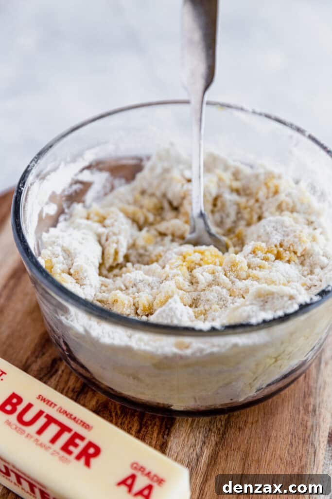 The dough for the cobbler topping being mixed in a glass bowl, with a stick of butter nearby