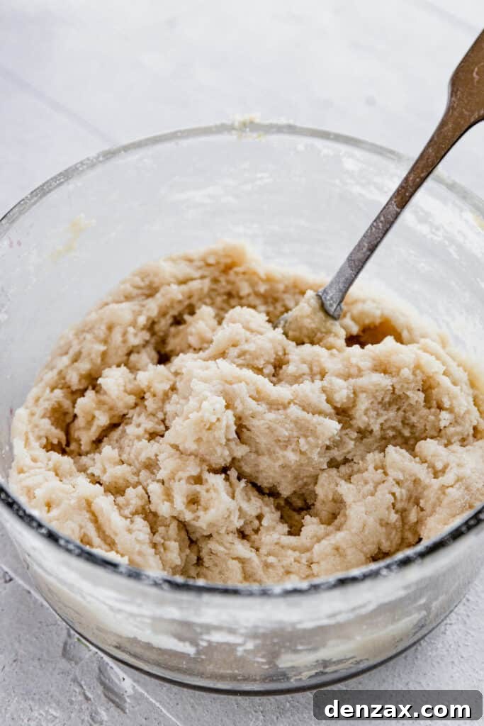 Close-up of the crumbly dough for the cobbler topping in a glass bowl with a metal spoon