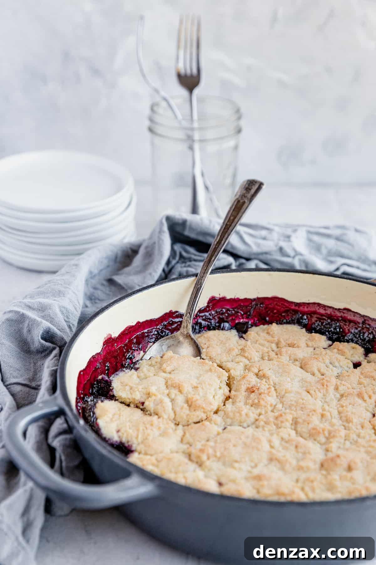 A freshly baked Blueberry Rhubarb Cobbler in a baking pan, with a metal spoon scooping out a portion