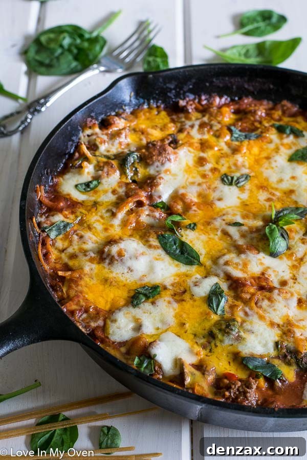 A large skillet filled with creamy linguine pasta, rich meat sauce, vibrant vegetables, and topped with golden-brown melted cheese.