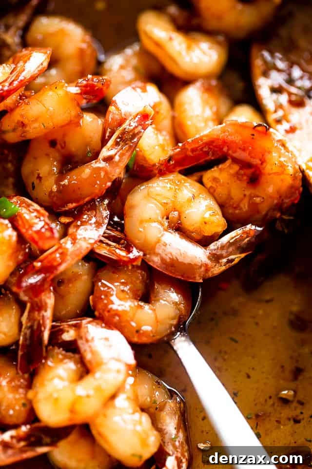 A hand stirring honey garlic shrimp in a cast iron skillet with a wooden spoon.