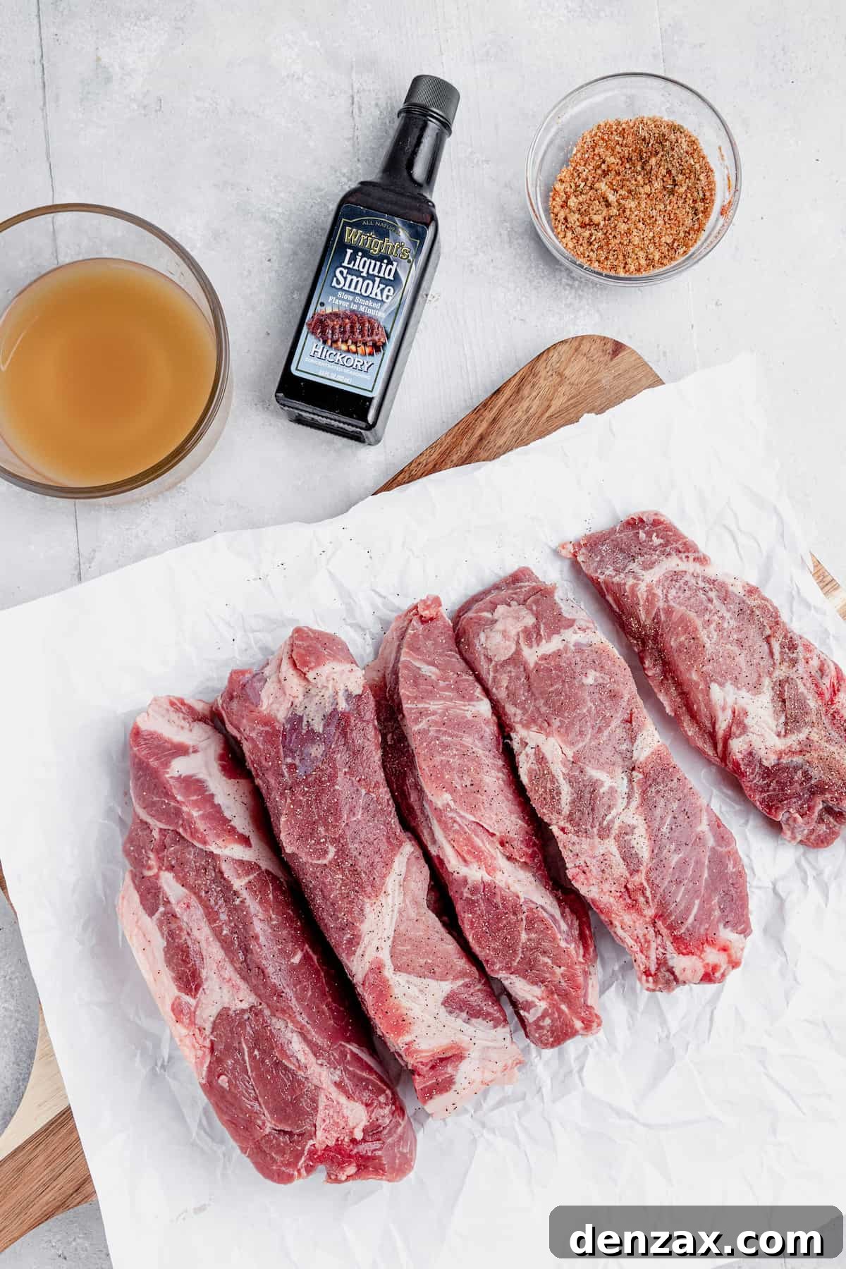 Uncooked Pork Ribs, a Bottle of Liquid Smoke and More of the Rib Ingredients on a Countertop, neatly arranged for preparation.