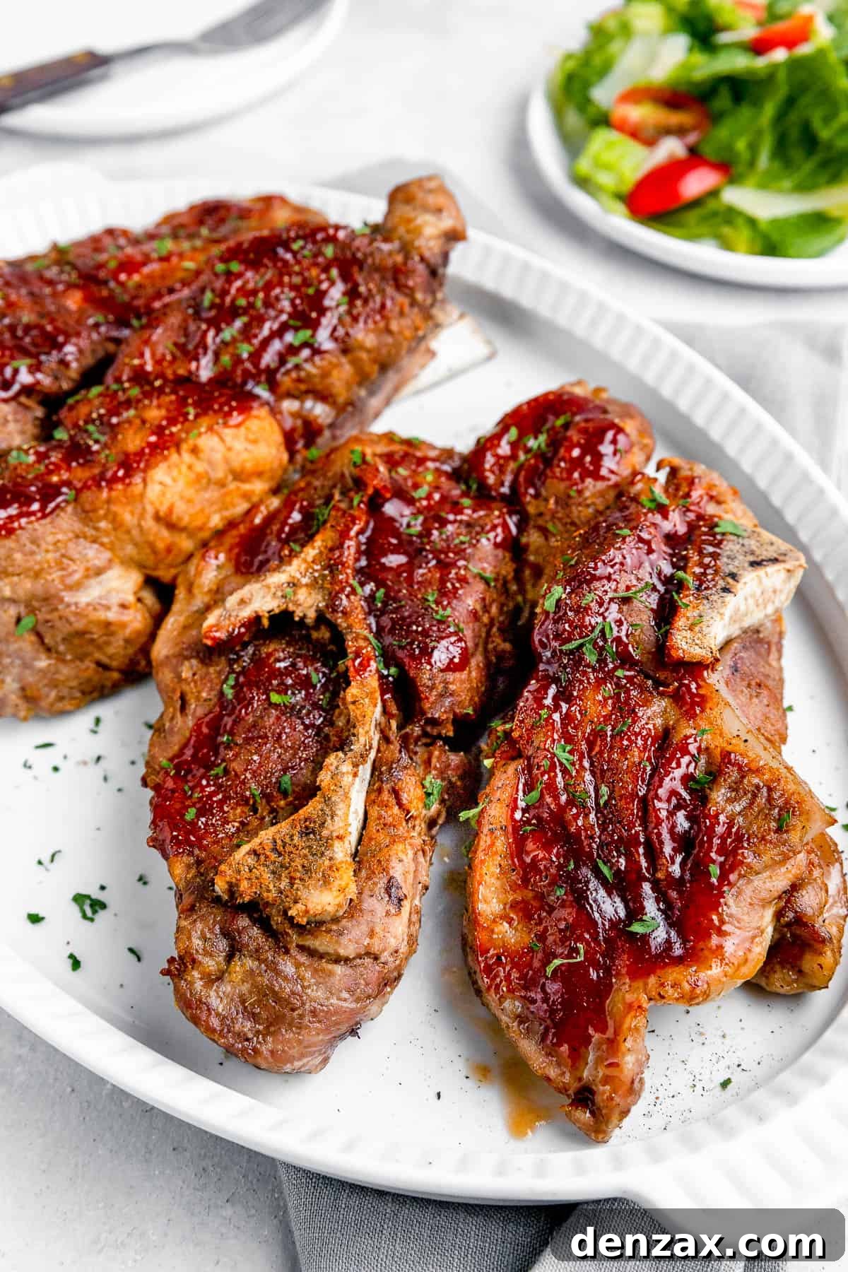 Side shot of Instant Pot Ribs on a White Serving Platter with a Small Salad in the Background, ready to be enjoyed.