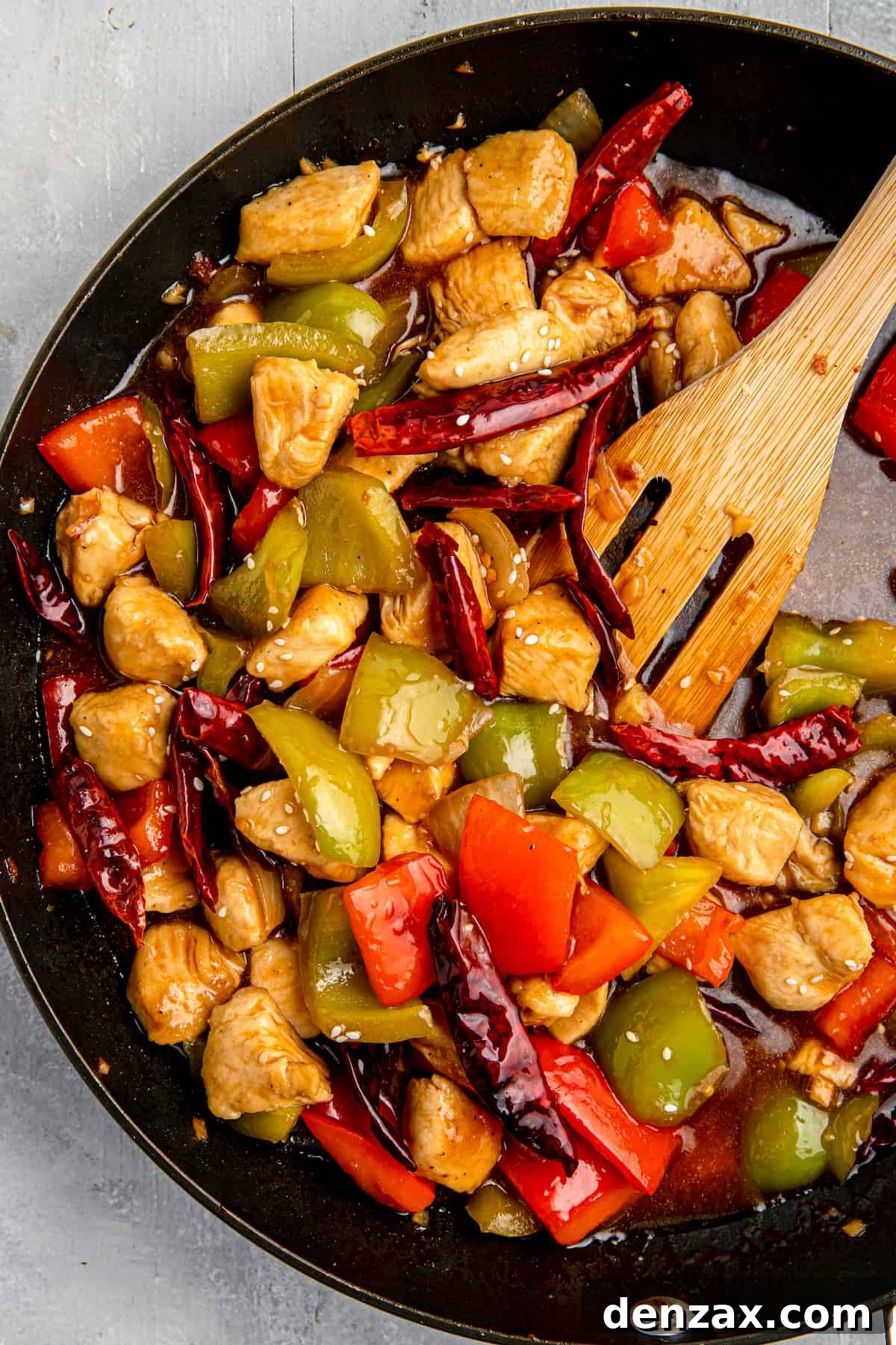Szechuan chicken stir-fry in a cast-iron skillet with a wooden spatula, ready to be served.