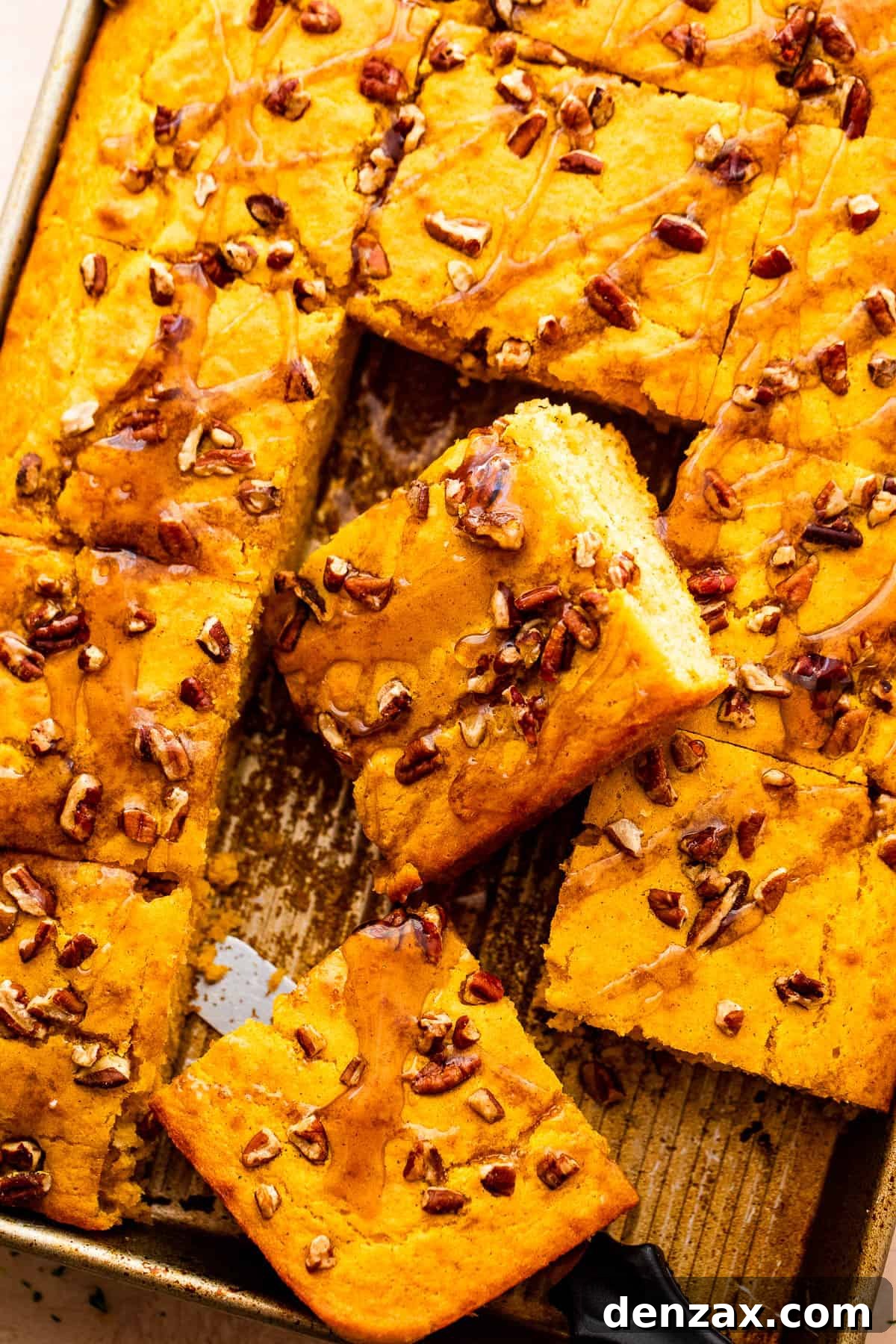 An overhead shot showcasing a full sheet pan of golden-brown pumpkin pancakes, cut into squares, ready to be served. Some squares are topped with chopped pecans.