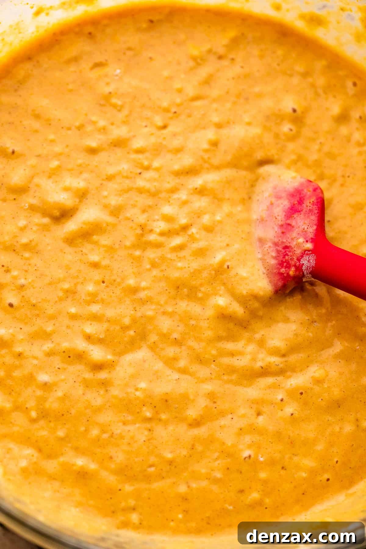 Close-up shot of a whisk stirring light orange pumpkin pancake batter in a large mixing bowl.