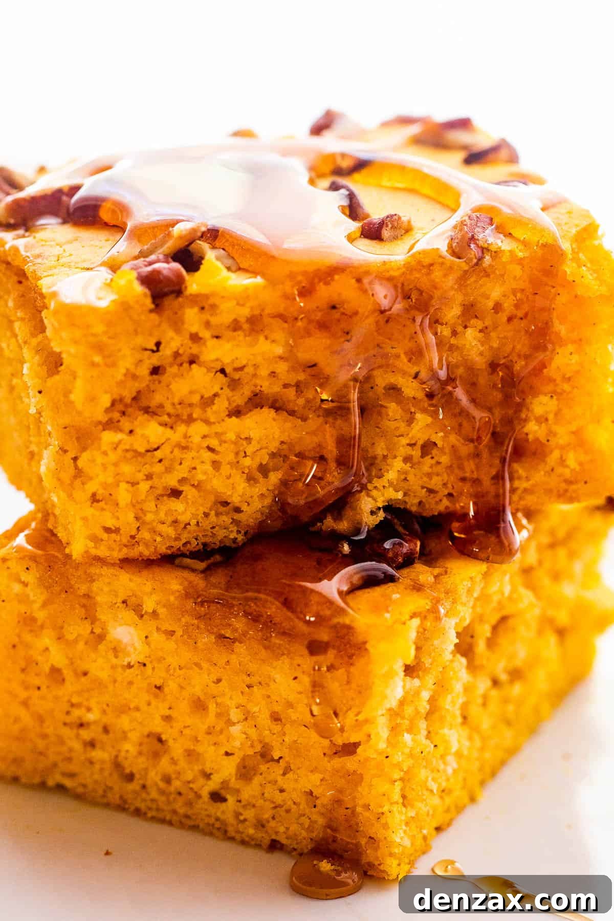 Two fluffy sheet pan pumpkin pancakes stacked neatly, with a dusting of powdered sugar and a dollop of whipped cream, on a white plate.